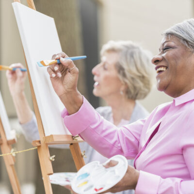 Two senior women having fun painting in art class